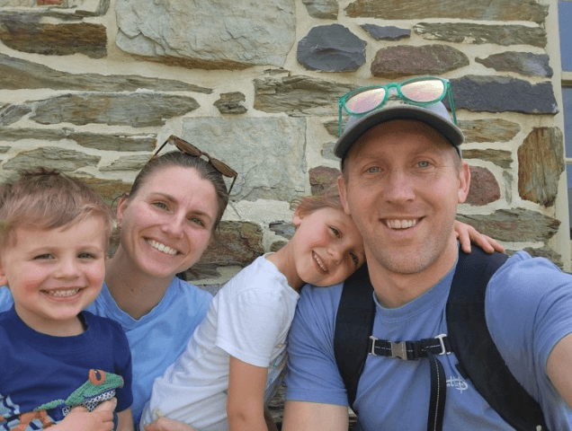Molly, her husband, and their two children smiling for a group picture in front of a stone wall.